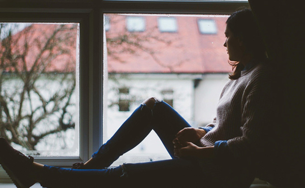 Young woman sitting by window looking out.
